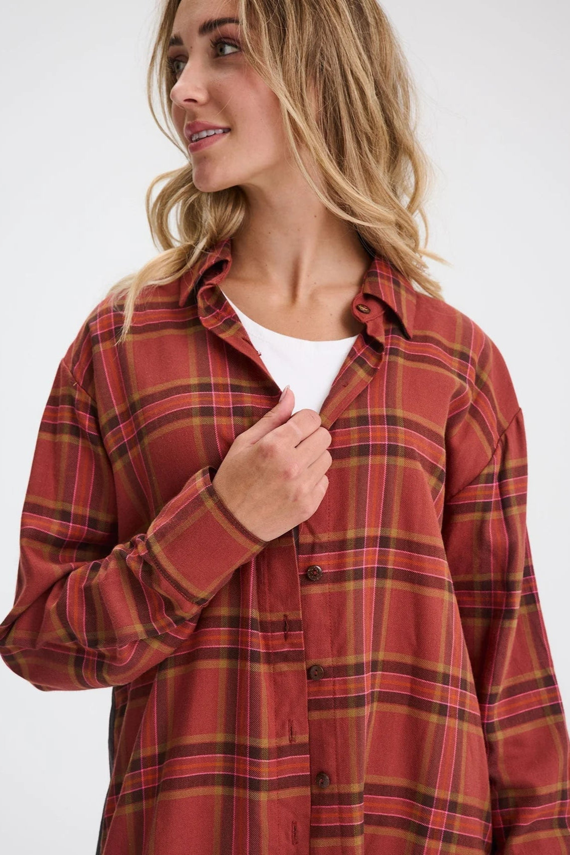 Waist up view of a woman wearing the Donnacona Shirt Dress by Message Factory in Rust Check, a knee-length dress with a button front and collar. She is wearing it open over a white t-shirt and standing in front of a white background. 