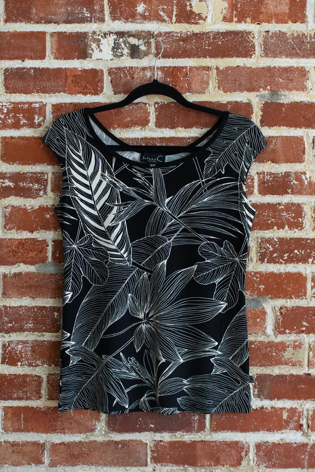 The Sol Top from Marie C in Black with Print, a reversible cap sleeve tee, is shown hanging vertically in front of a brick wall.