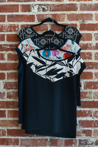 The Pepita Top from Marie C, a reversible t-shirt with a printed fabric yoke on one side, is shown hanging on a brick wall. From top to bottom the colours are: Black with Print, Navy, and Black and White. 