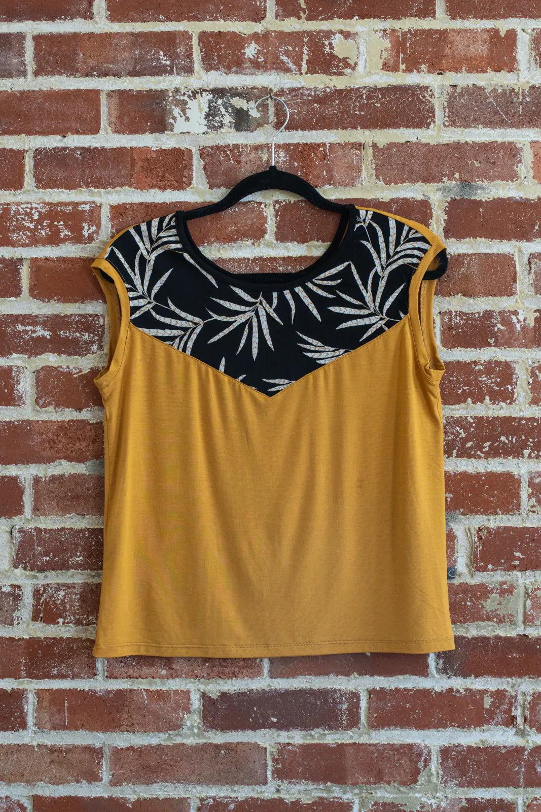 The Pepita Top from Marie C, a reversible t-shirt with a printed fabric yoke on one side, in Yellow, is shown hanging on a brick wall.