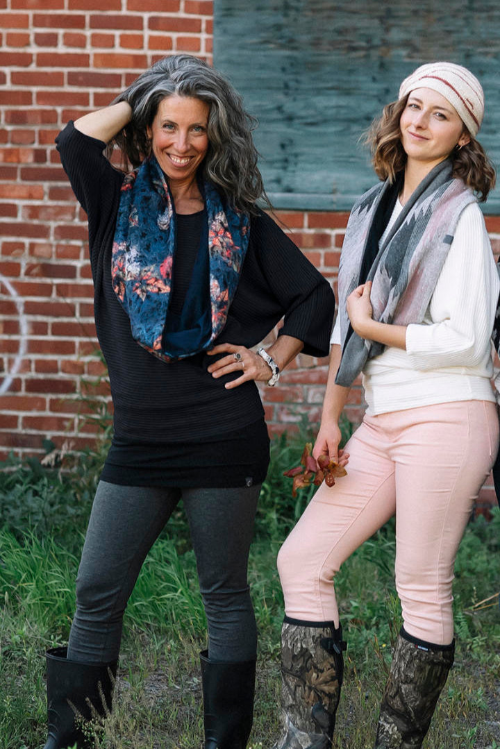 Two women wearing the Perla Top by Marie C,  one in Ivory and one in Black, with a wide round neck, 3/4 batwing sleeves, and fitted waist in ribbed knit fabric. They wear the tops with jeans and are standing outside. 