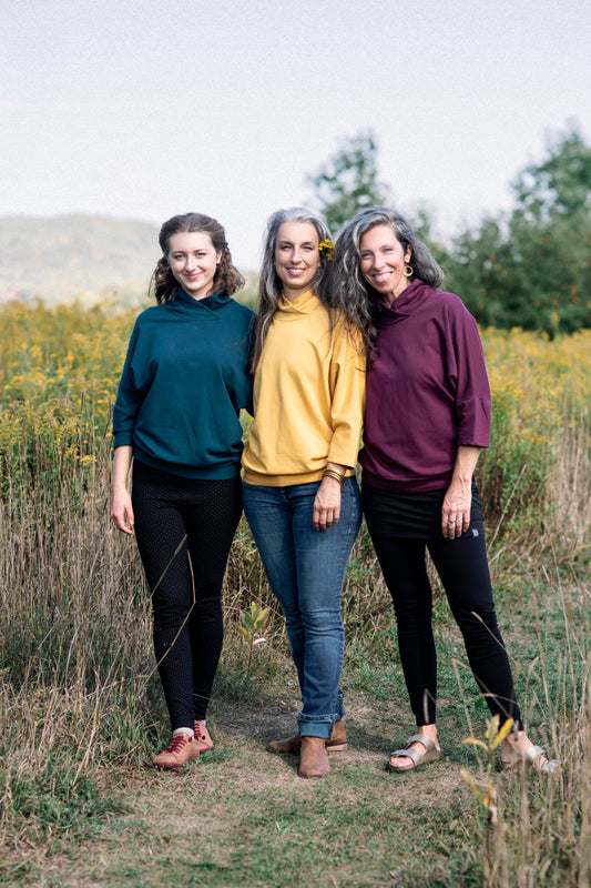 Three women wearing the BeAAA Sweater by Marie C in Everglade, Yellow and Wine, standing in a field 