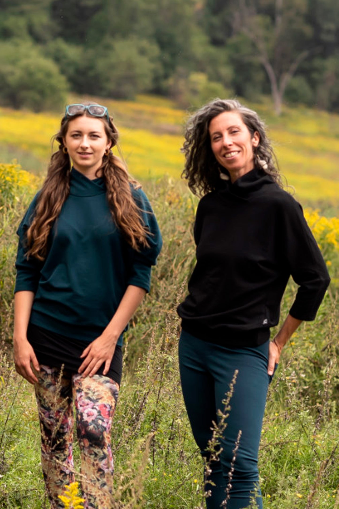 A woman wearing the Beaaa Top by Marie C in Everglade,  and a woman wearing the Beaaa Top by Marie C in Black, standing in a field