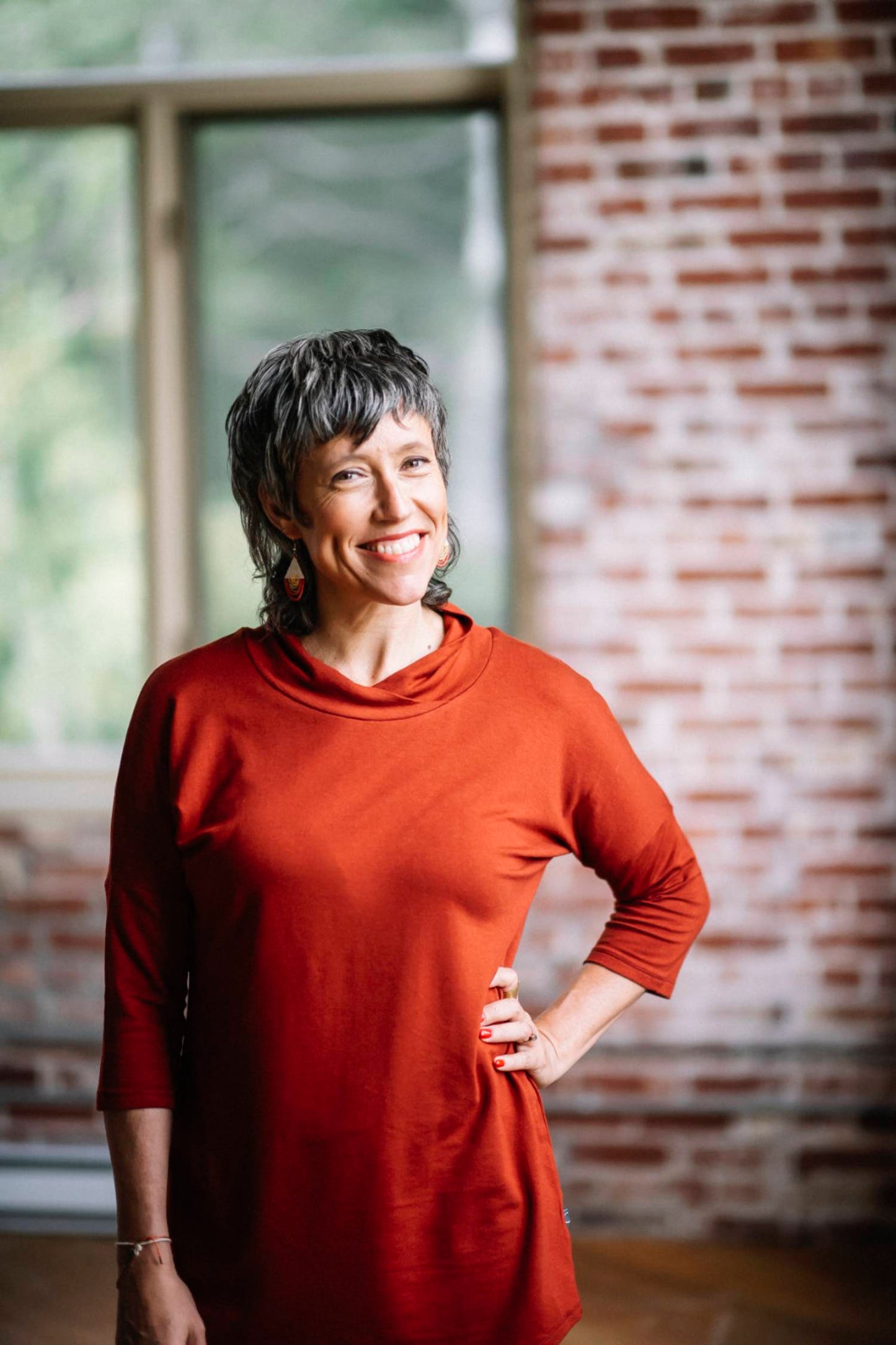  A woman wearing Juliana Tunic by Marie C in Rust, standing in front of a brick wall 