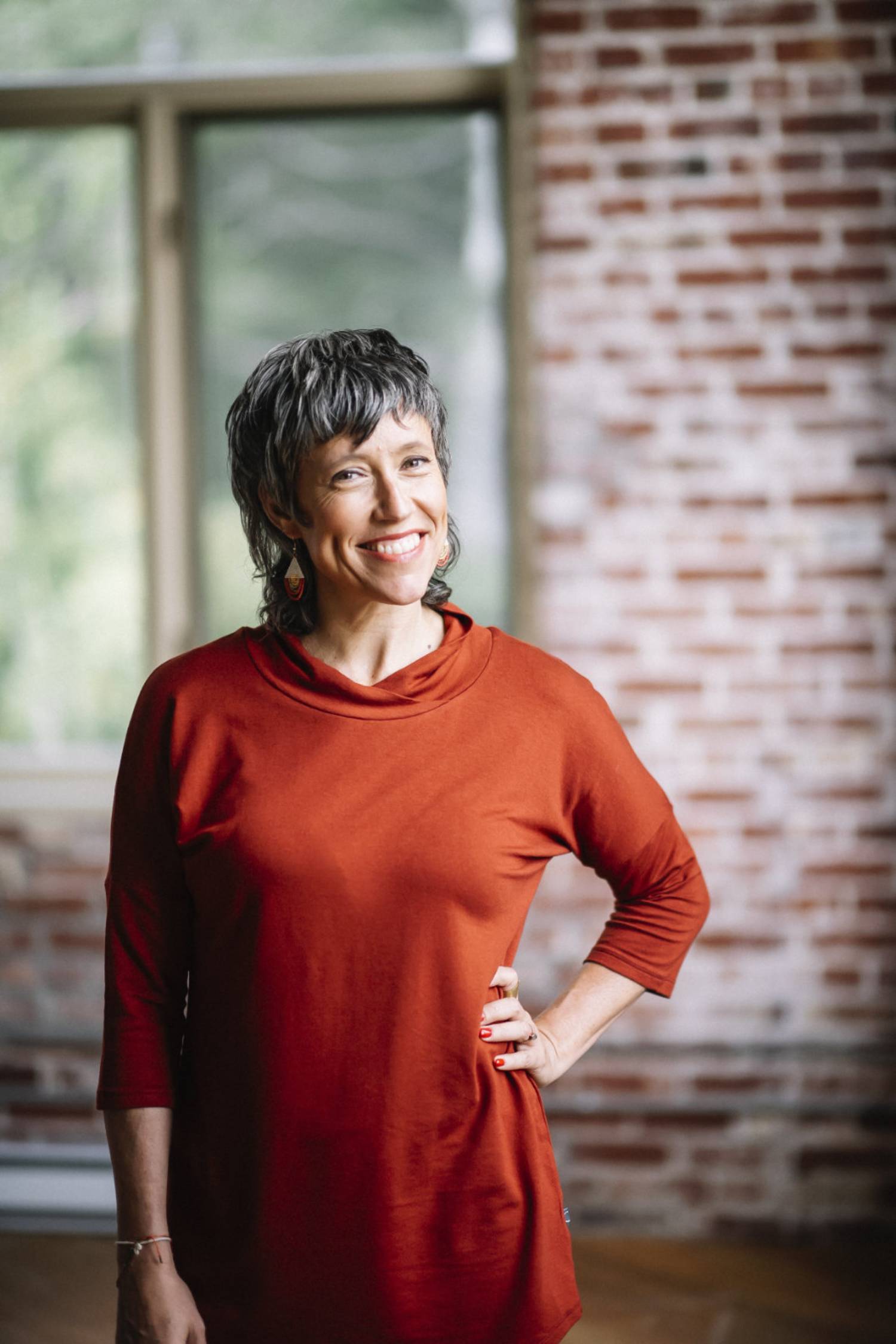  A woman wearing Juliana Tunic by Marie C in Rust, standing in front of a brick wall 