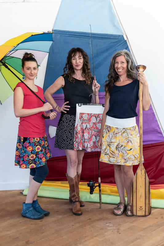 Three women wearing the Soleil Skirt by Marie C, with Sol Tops, standing indoors in front of a sail and outdoor accessories. 