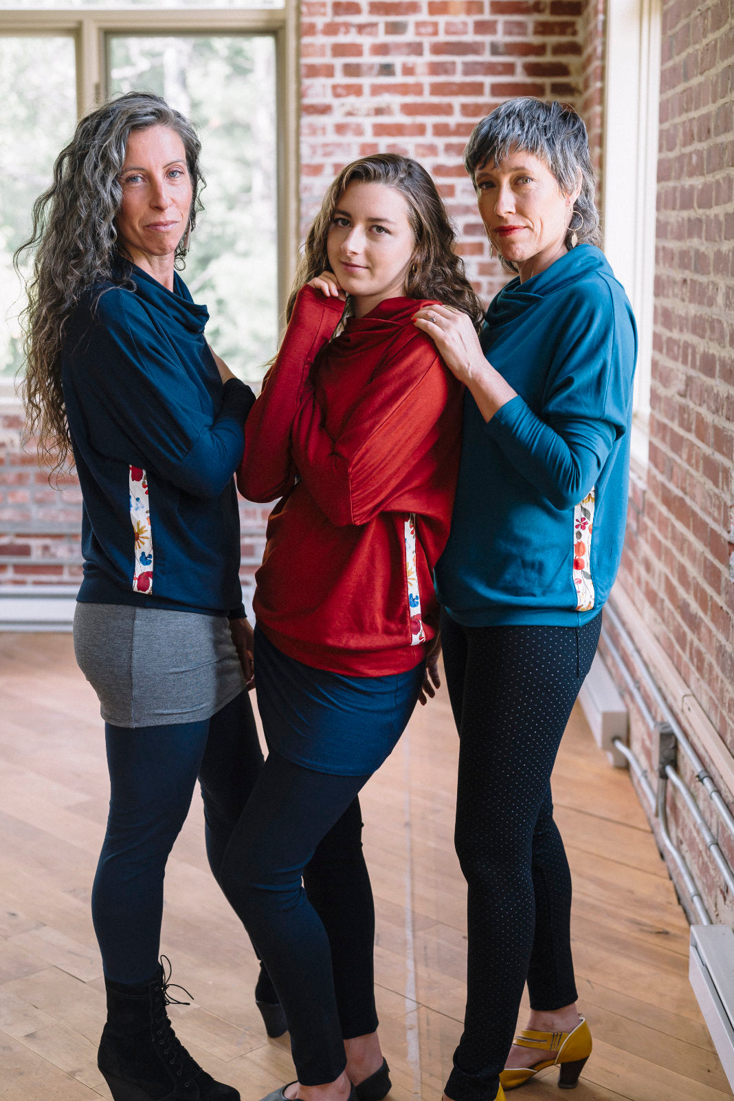 Three women wearing the Mimoso Top by Marie C in Rust, Teal, and Navy, standing in front of a brick wall