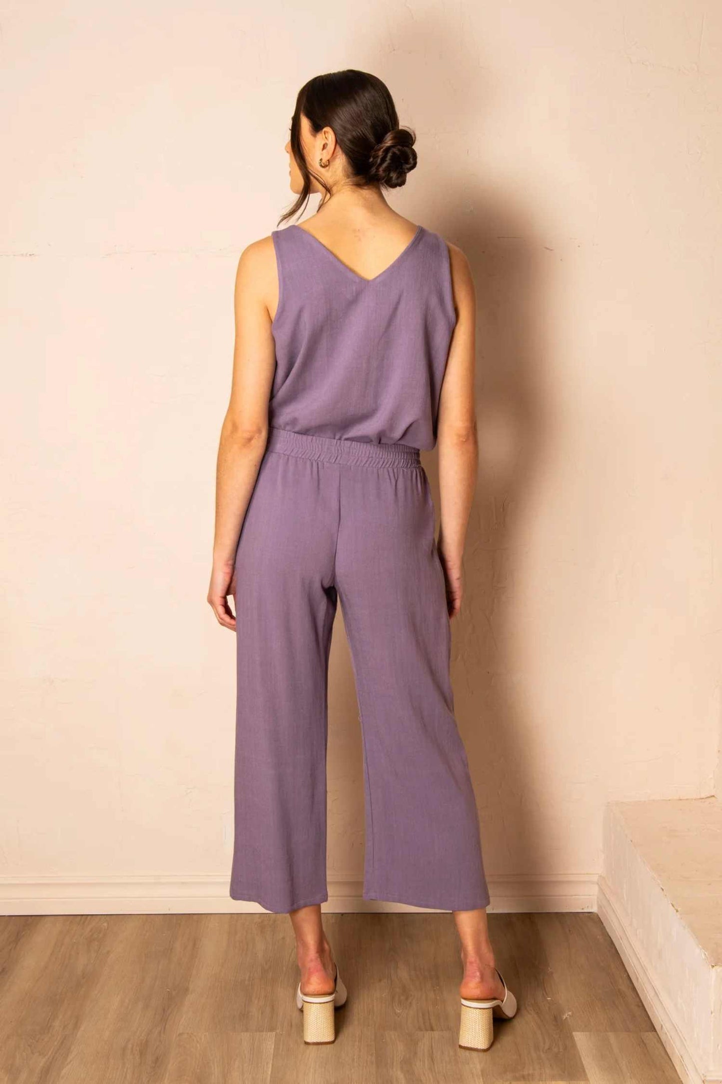 Back view photo of a woman wearing the Serenity Pants by Cherry Bobin in Mauve, standing in front of a wall 