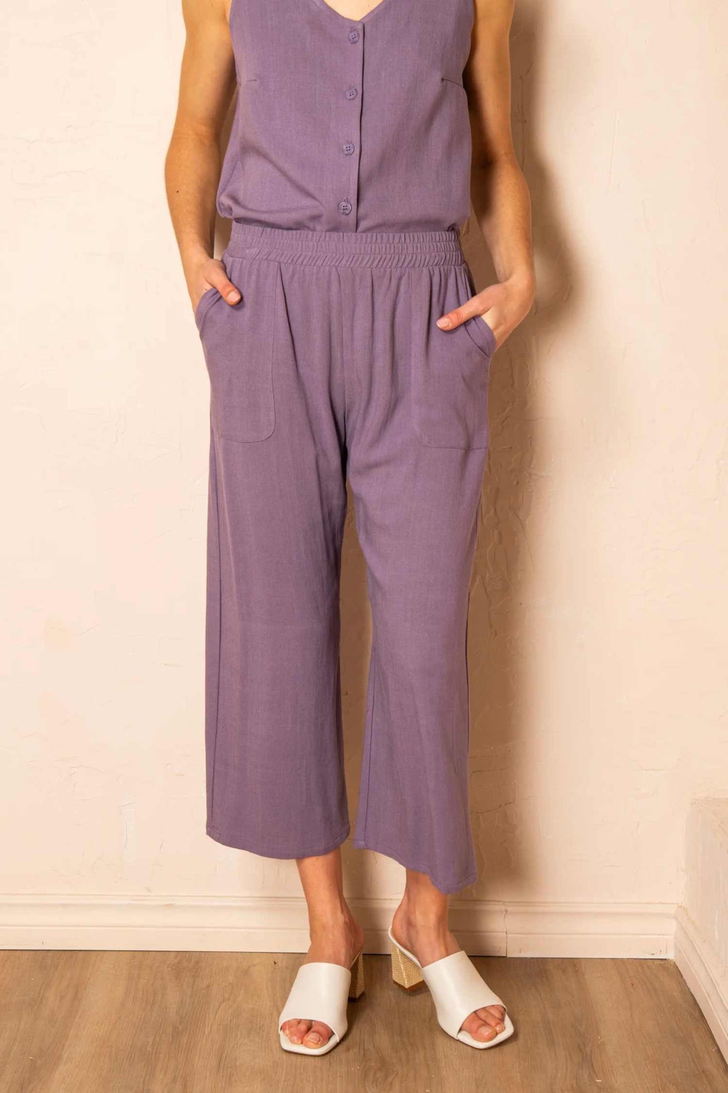 Close-up view  of a woman wearing the Serenity Pants by Cherry Bobin in Mauve, standing in front of a wall 