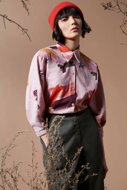 A woman wearing the Juliette Top by Melow in Sobel Print, featuring a pale pink background with splashes of colour.  The shirt has a blouse collar, button front, and 3/4 length puff sleeves. 