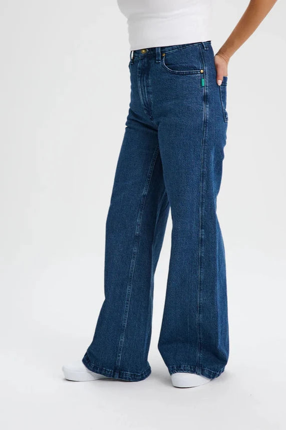 Waist down view of a woman wearing the Hochelaga Flared Leg Denim Pants by Message Factory, a wide leg jean made from organic cotton, with a white tee. She is standing in front of a white background. 