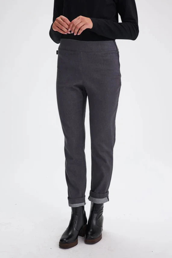 Chest-down view of a woman wearing the Potton Pants by Message Factory in Gray Denim,  slim cut pants in stretchy denim with a wide waistband and a side zipper, made from recycled cotton and polyester. She's standing in front of a white background. 