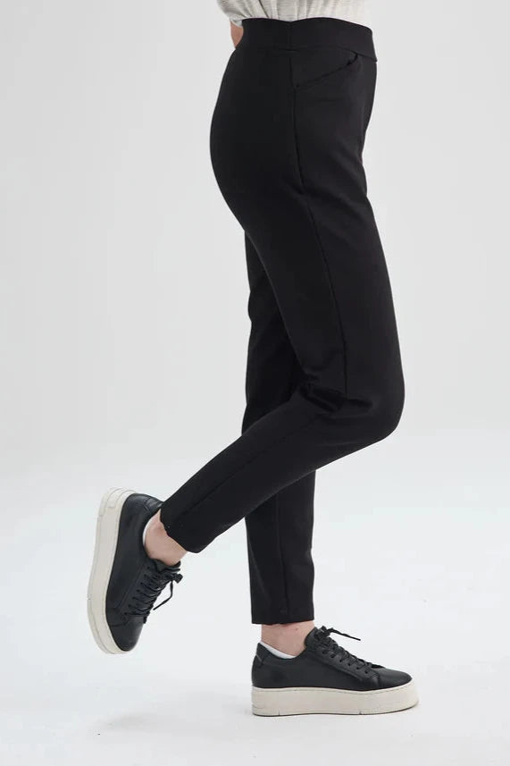 Side waist-down view of the Sherbrooke Pants by Message Factory in Black, pull-on semi-fitted pants with side pockets made from Lenzing Ecovero viscose. She is standing in front of a white background. 