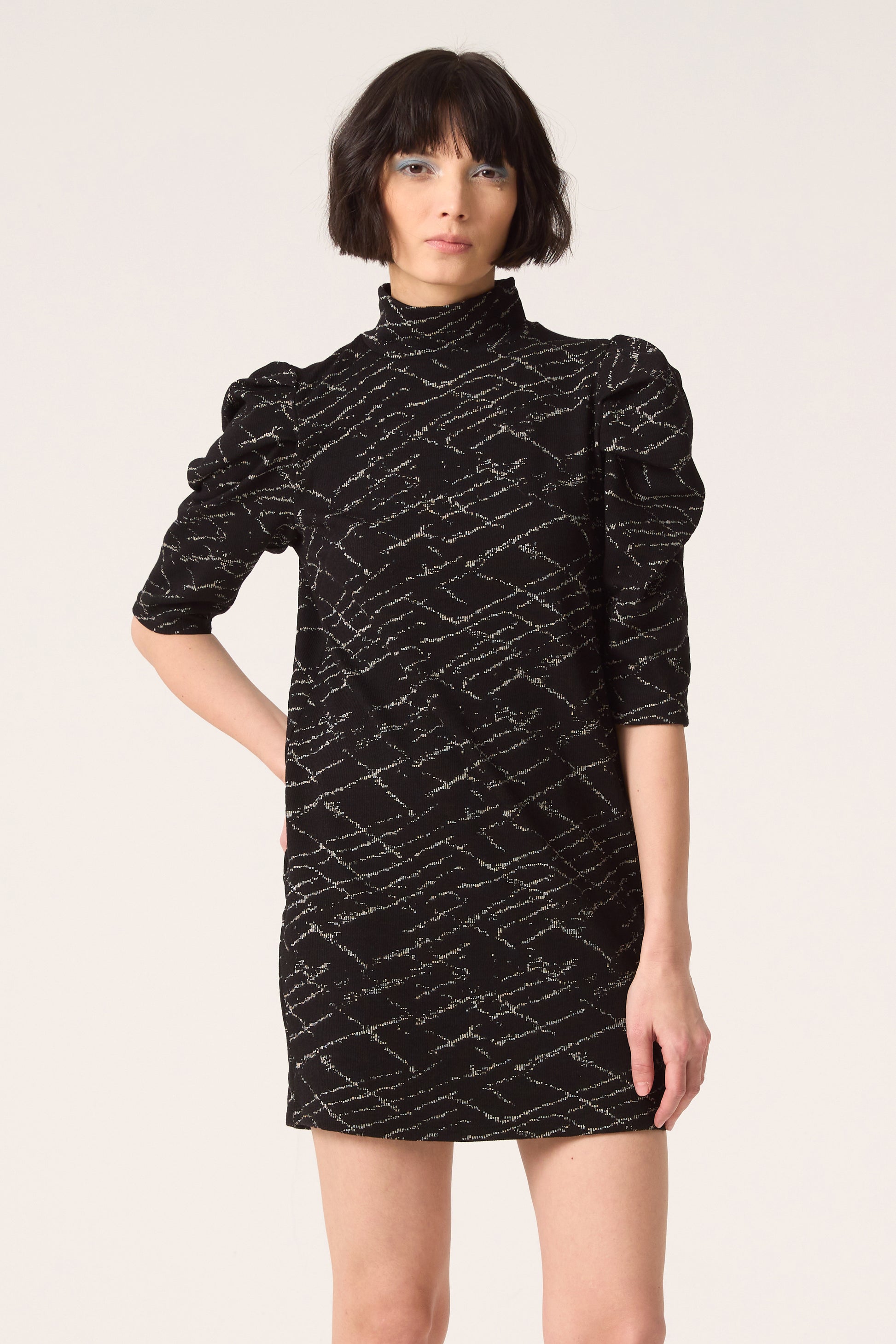 3/4 shot of a woman wearing the Nostalgia Dress by Cokluch in Black, standing in front of a white  background.