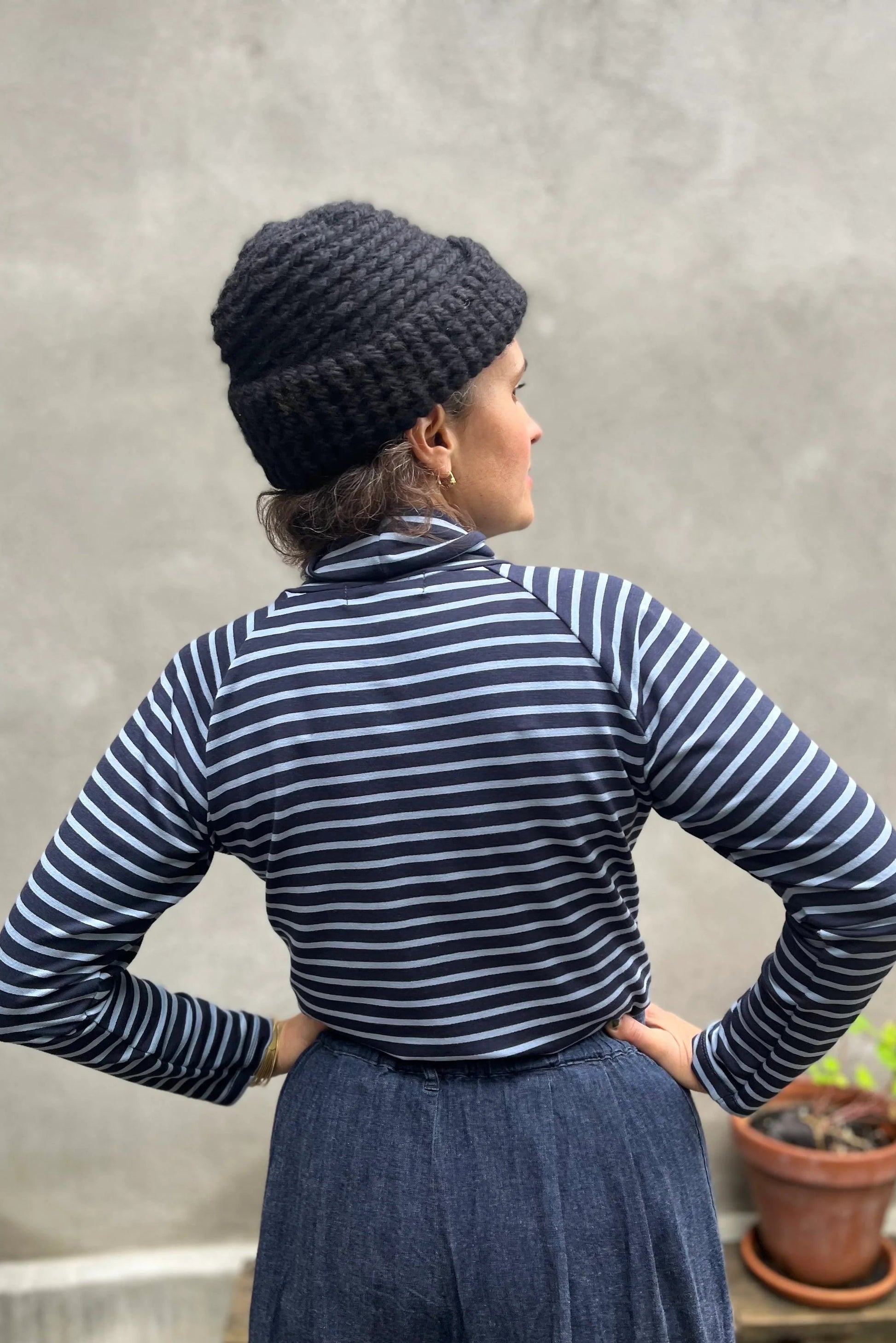 A woman wearing the Oris Raglan Turtleneck by Kazak in Blue Stripe. She is wearing it with jeans and standing outside. 