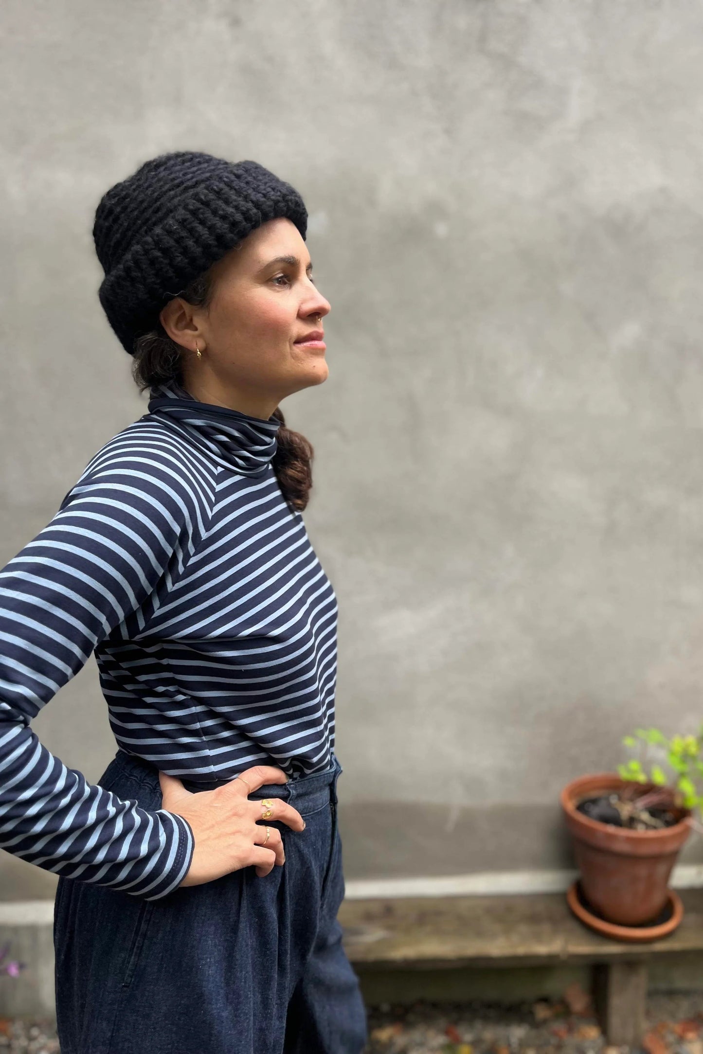 A woman wearing the Oris Raglan Turtleneck by Kazak in Blue Stripe. She is wearing it with jeans and standing outside. 