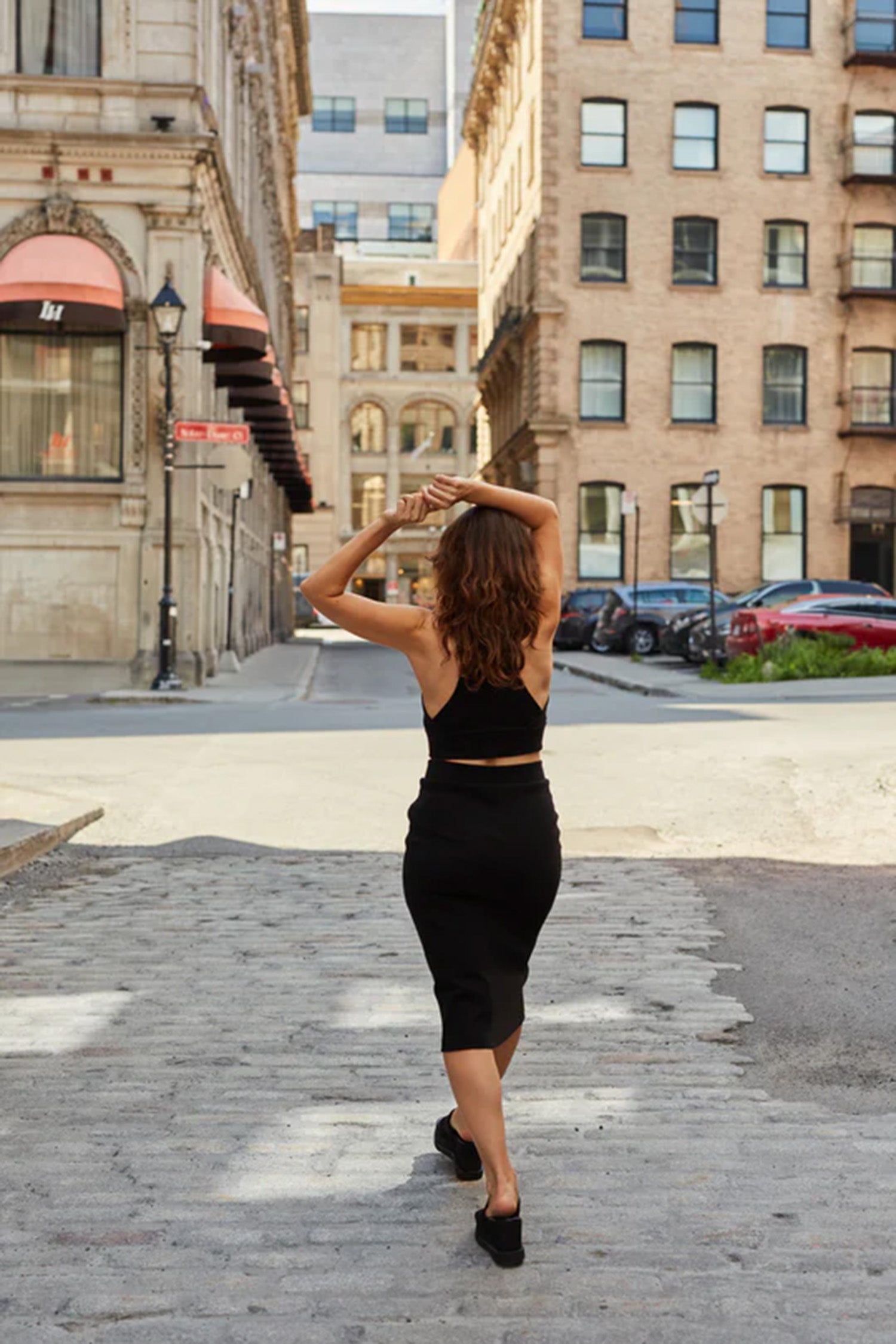 Back view of a woman wearing the Osaka Tank Top and Cartagena Skirt by MAS in Pepper, walking down a cobblestone street 