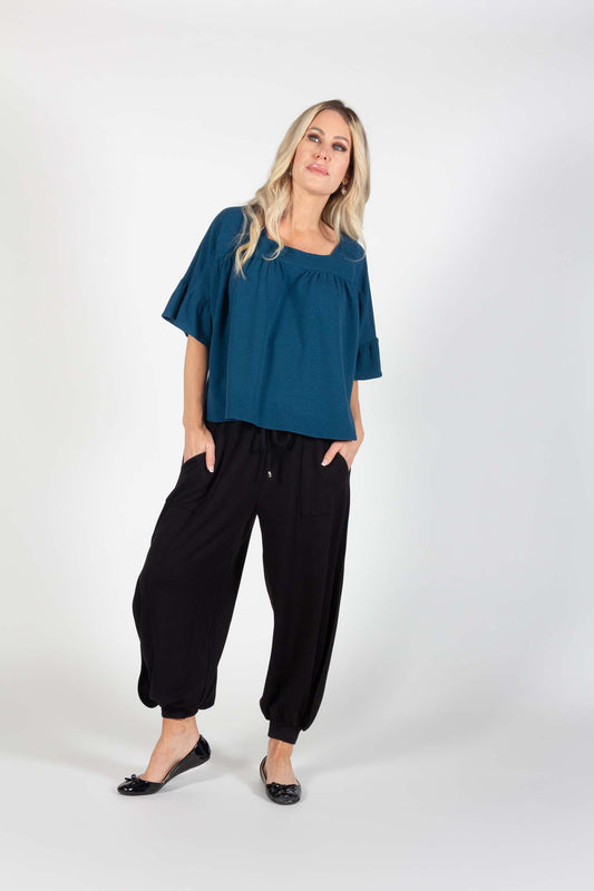 A woman wearing the Calvin Top by Pure Essence in Navy with black harem pants, standing in front of a white background