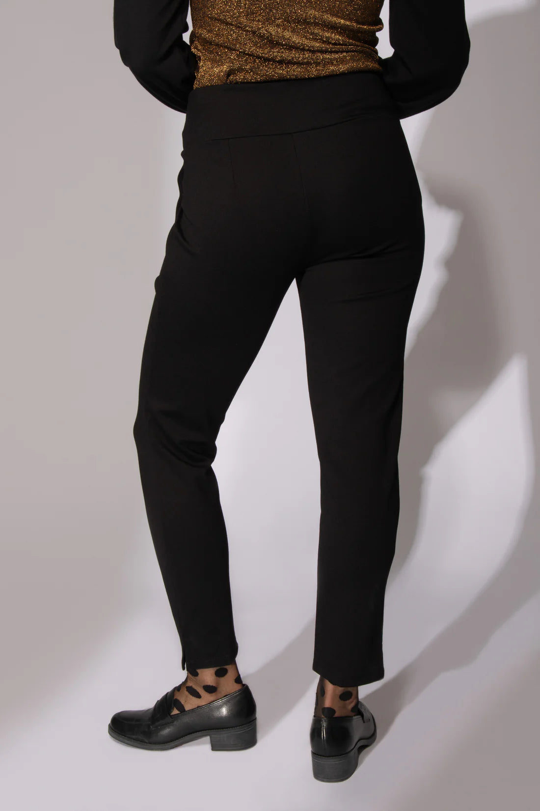 Back waist-down view of a woman wearing the I Follow You Pants by Eve Lavoie in Black, standing in front of a white background 