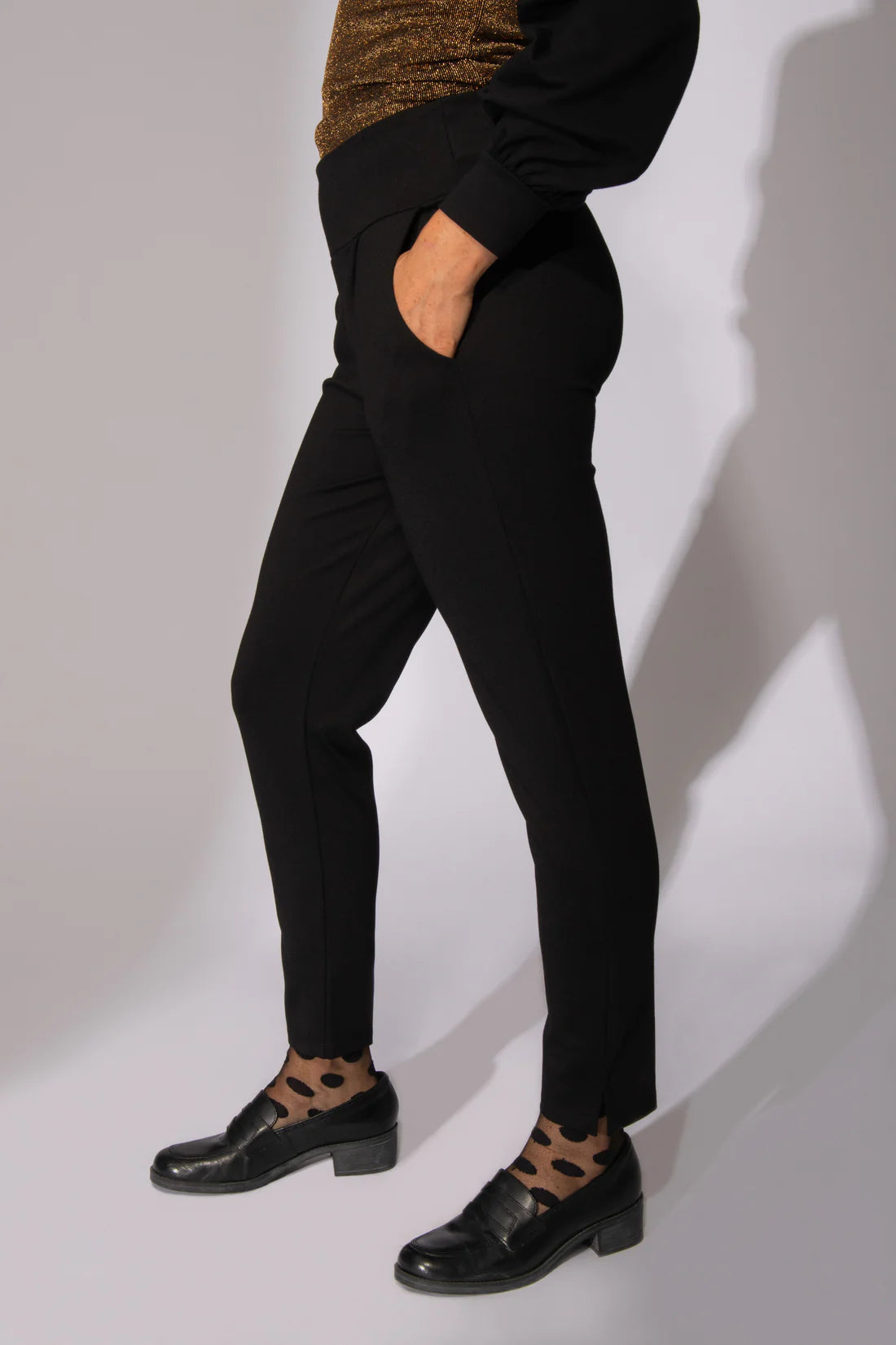 Waist-down, side view shot of a woman wearing the I Follow You Pants by Eve Lavoie in Black, standing in front of a white background 