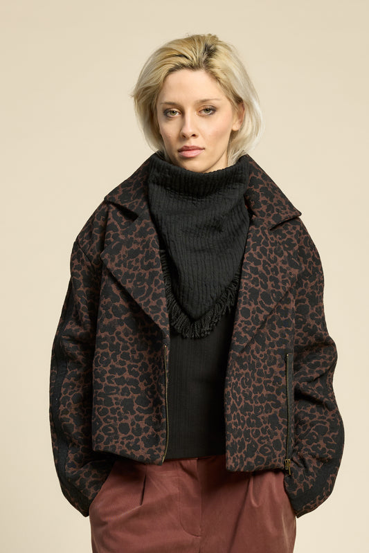 Waist up view of a woman wearing the Perfect Day Jacket by Cokluch in Cappuccino  Leopard, a motorcycle style jacket that's double breasted with a wide collar and zip front. She is wearing it with a black top and brown pants and standing in front of a beige background.