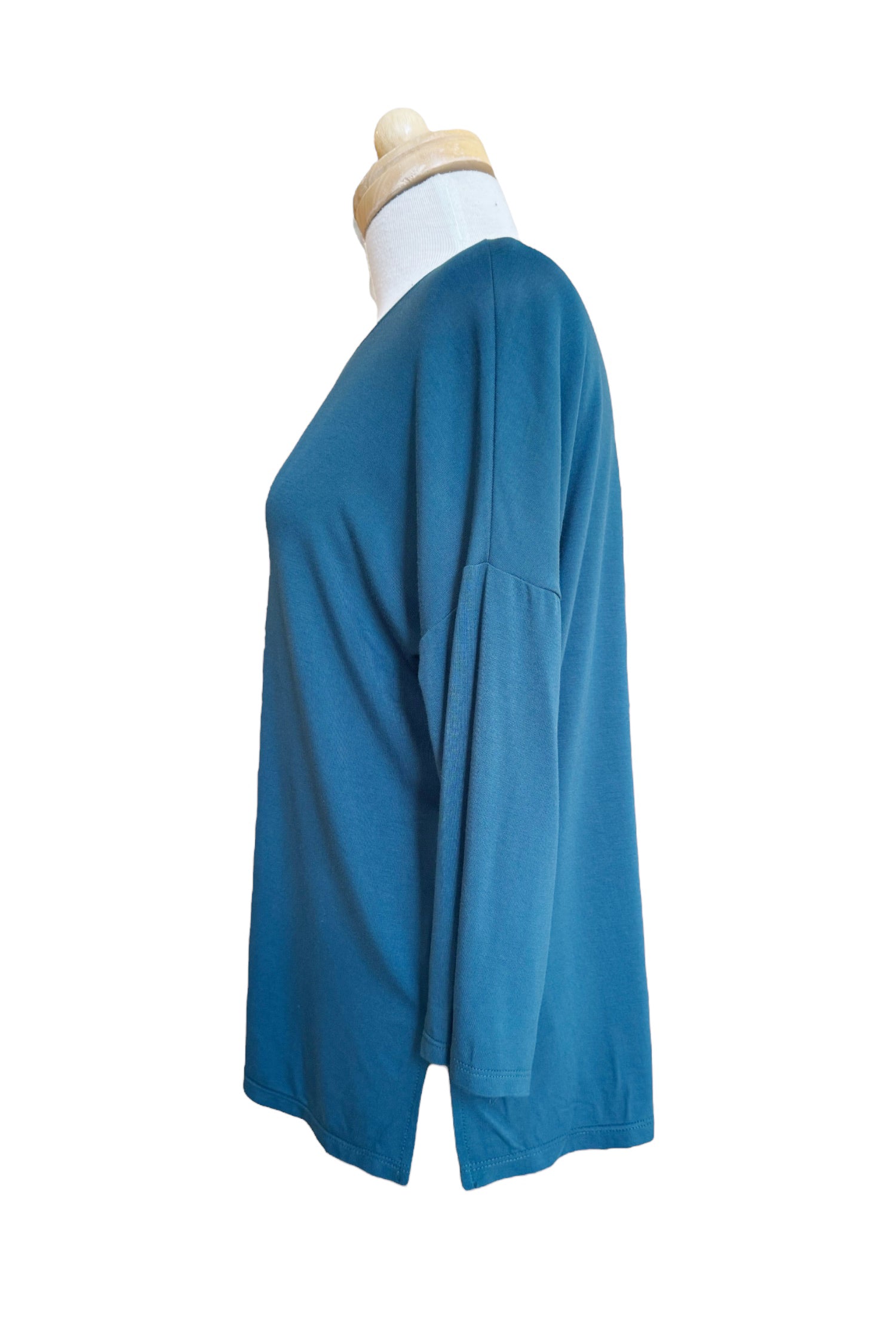 A side view of the Emmy Top by Moovment in Teal, with a boat neck, 3/4 sleeves, and side slits, is shown on a mannequin in front of a white background. 