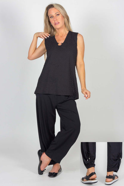 A woman wearing the Celeste Harem Capri by Pure Essence in Black, standing in front of a white background. The ruching and tie detail at the back of the ankles is show in a small inset photo.