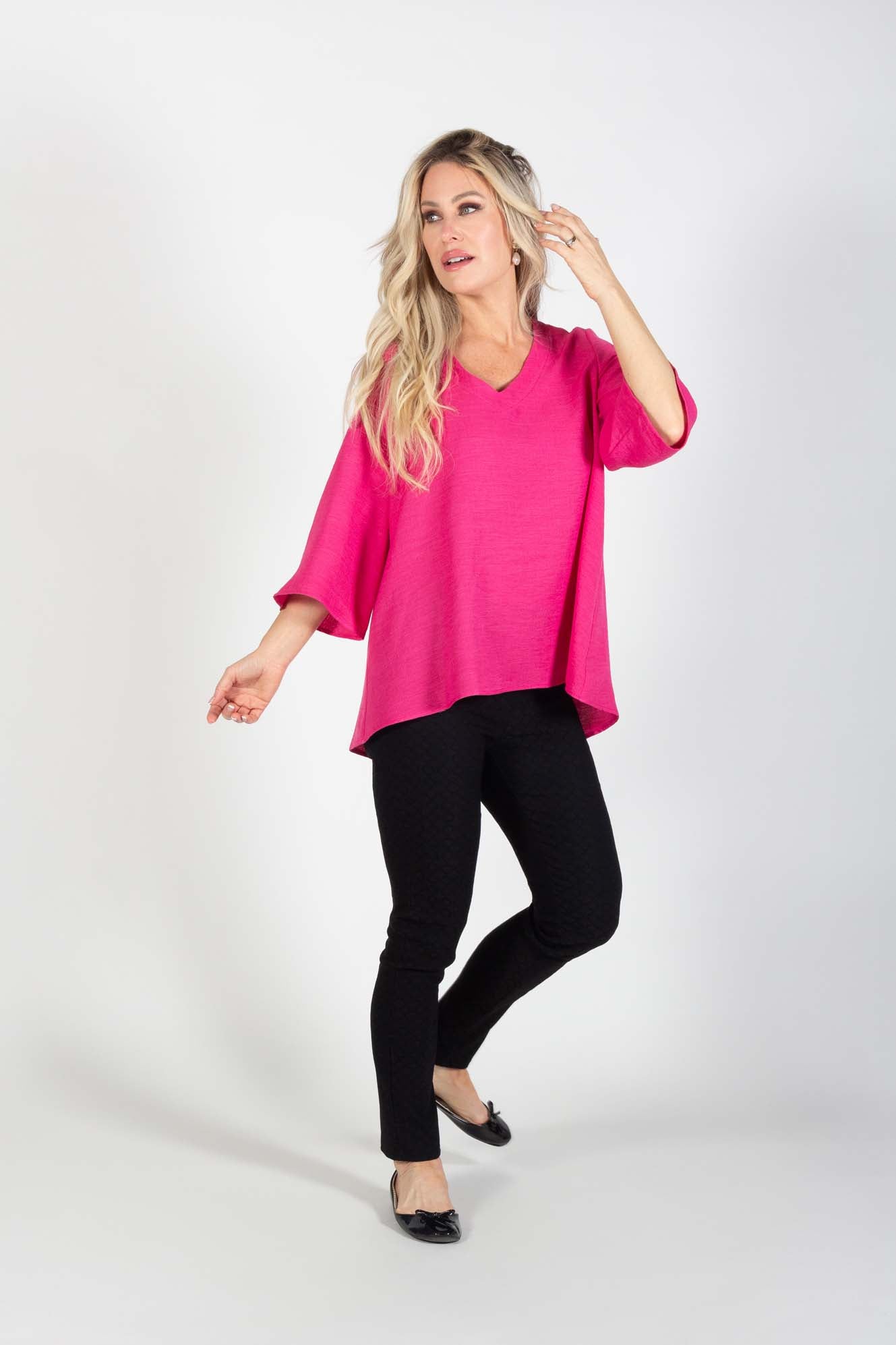 A woman wearing the Calypso Top by Pure Essence in Azalea with black pants standing in front of a white background
