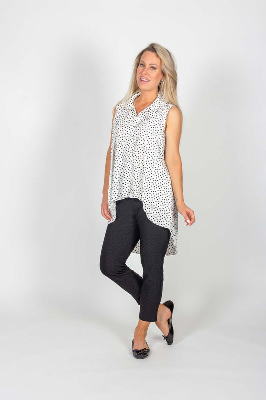 A woman wearing the Cambria Top by Pure Essence in Ivory with black polka dots, along with black pants, standing in front of a white background