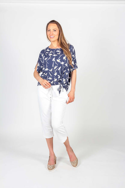 A woman wearing the Carter Top by Pure Essence in Navy Floral with white pants standing in front of a white background