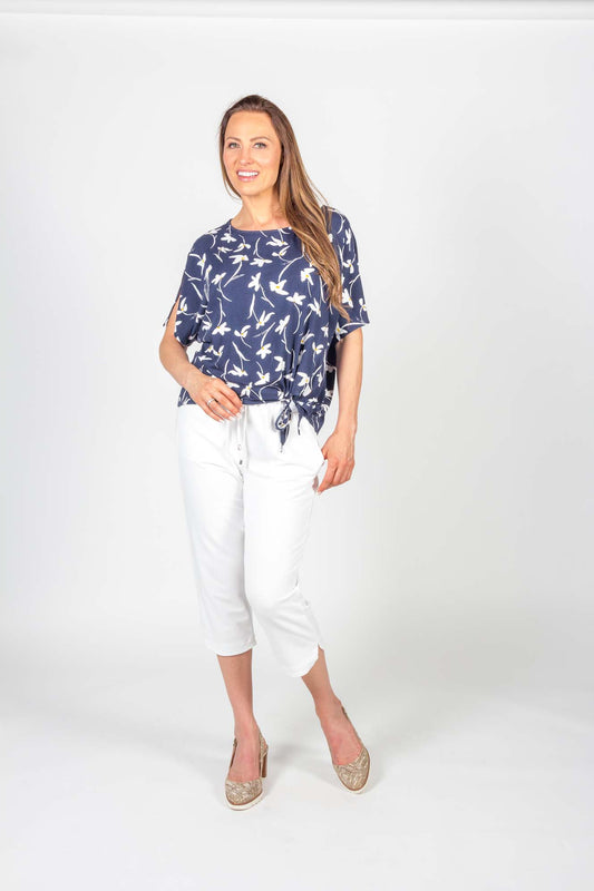 A woman wearing the Carter Top by Pure Essence in Navy Floral with white pants standing in front of a white background