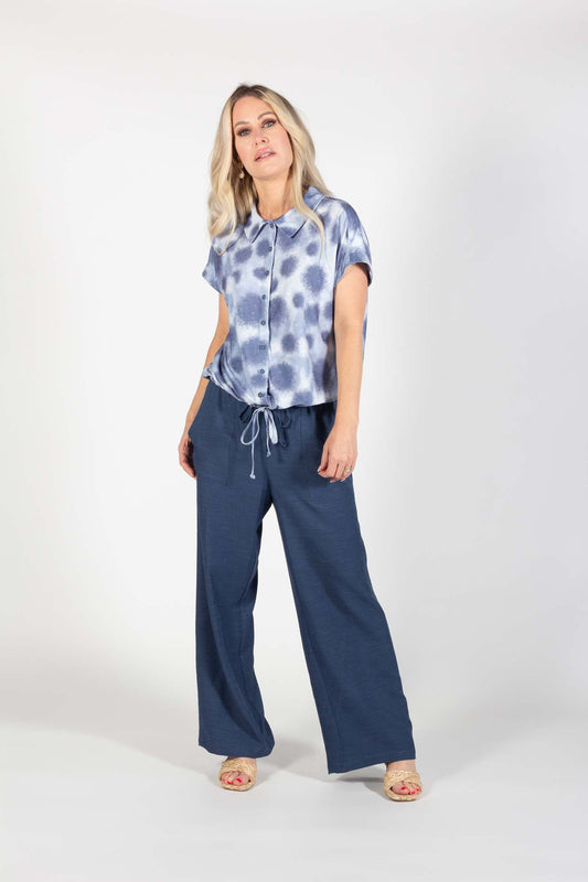 A woman wearing the Cedric Pants by Pure Essence in Indigo and a blue and white top stands in front of a white background 