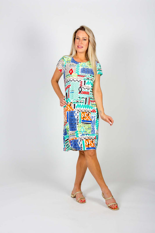 A woman wearing the Chastity Dress by Pure Essence in a geometric Aqua/Blue print stands in front of a white background 