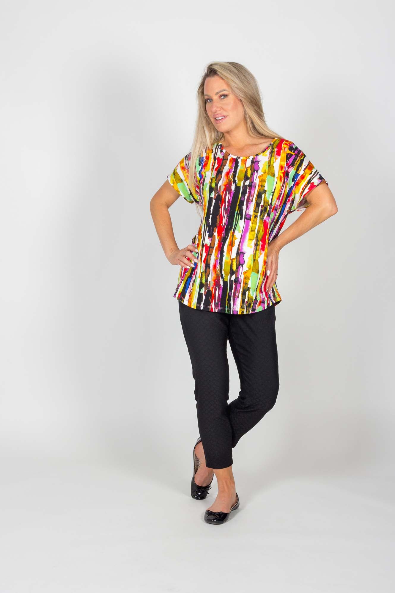 A woman wearing the Chichi Top by Pure Essence in Multicolour Print with the  Caroline Pant in Black is standing in front of a white background