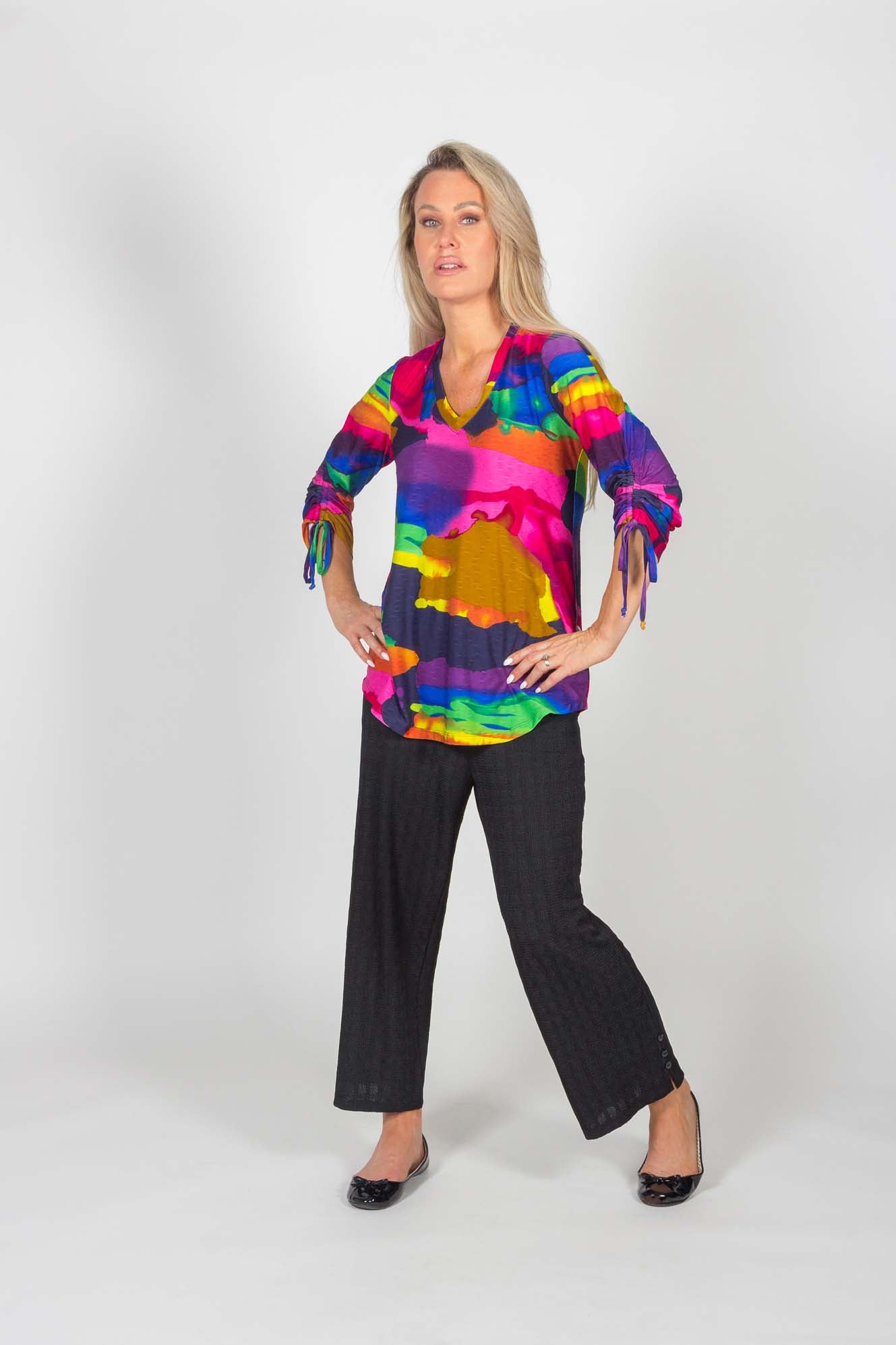 A woman wearing the Ciara Capri by Pure Essence in Black with a multicolour shirt stands in front of a white background 