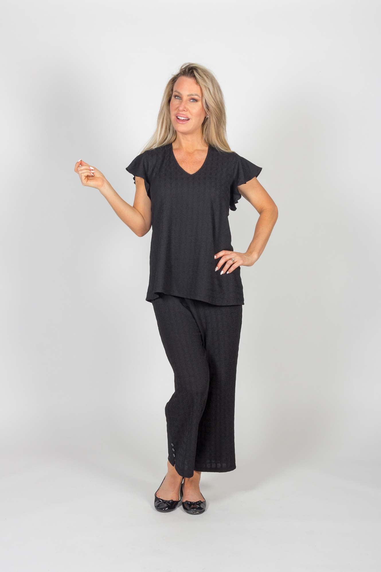 A woman wearing the Ciara Capri by Pure Essence in Black with a black top stands in front of a white background 