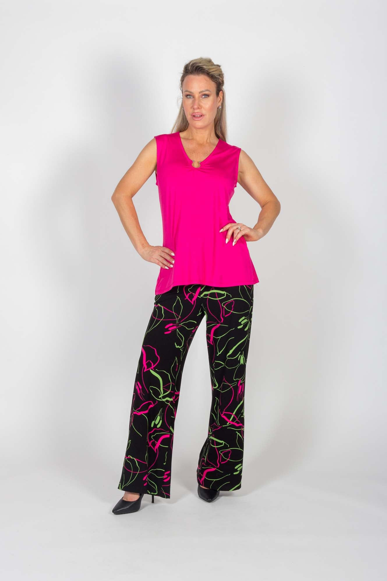 A woman wearing the Clarisse Pants by Pure Essence in Black/Pink/Green with a pink top standing in front of a white background