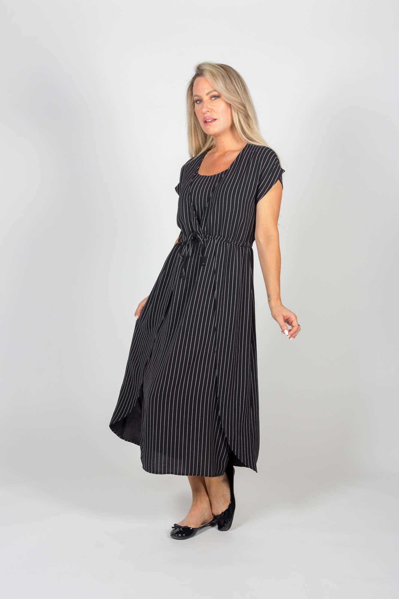 A woman wearing the Clementine Dress by Pure Essence in Black pinstripe stands in front of a white background