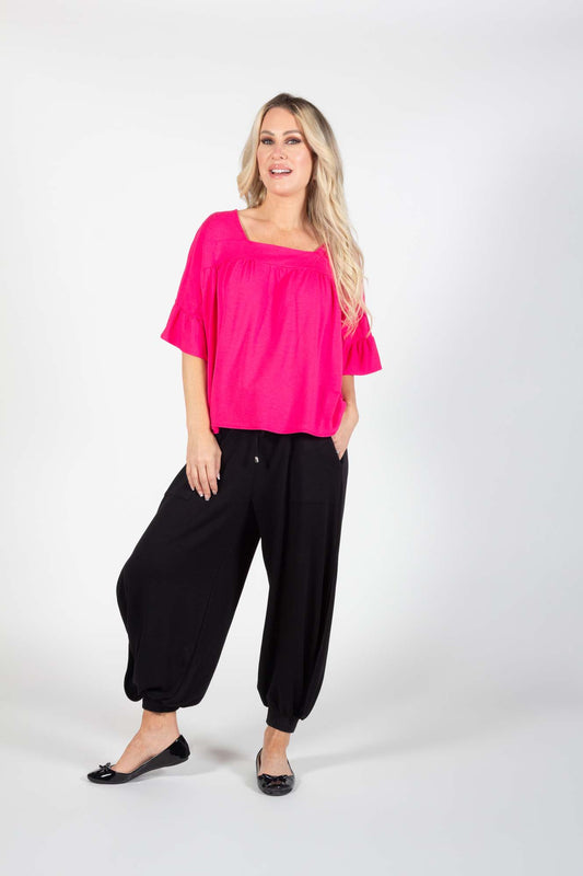 A woman wearing the Cooper Harem Pants by Pure Essence in Black with a hot pink top standing in front of a white background
