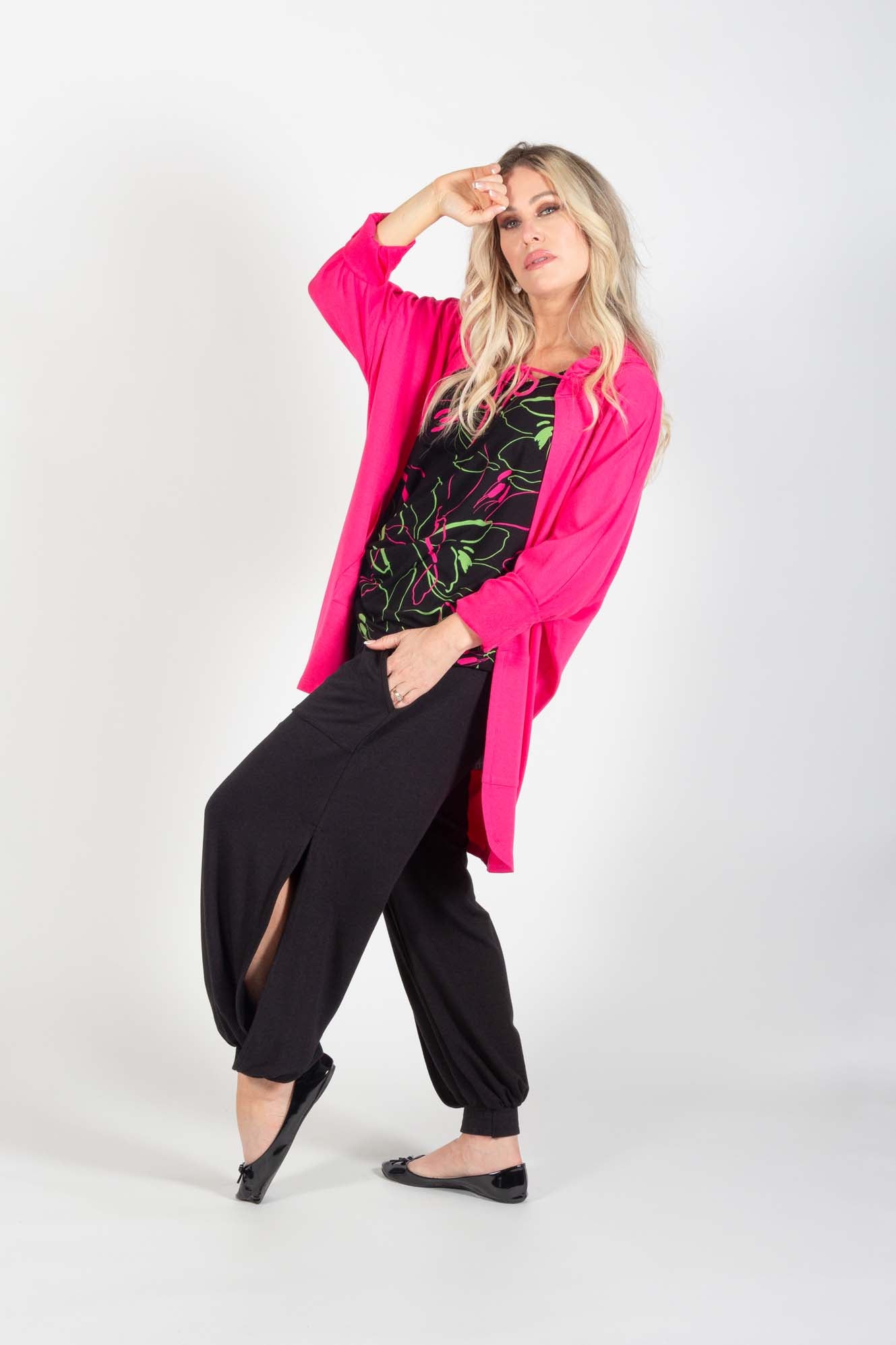 A side view of a woman wearing the Cooper Harem Pants by Pure Essence in Black with a hot pink top standing in front of a white background