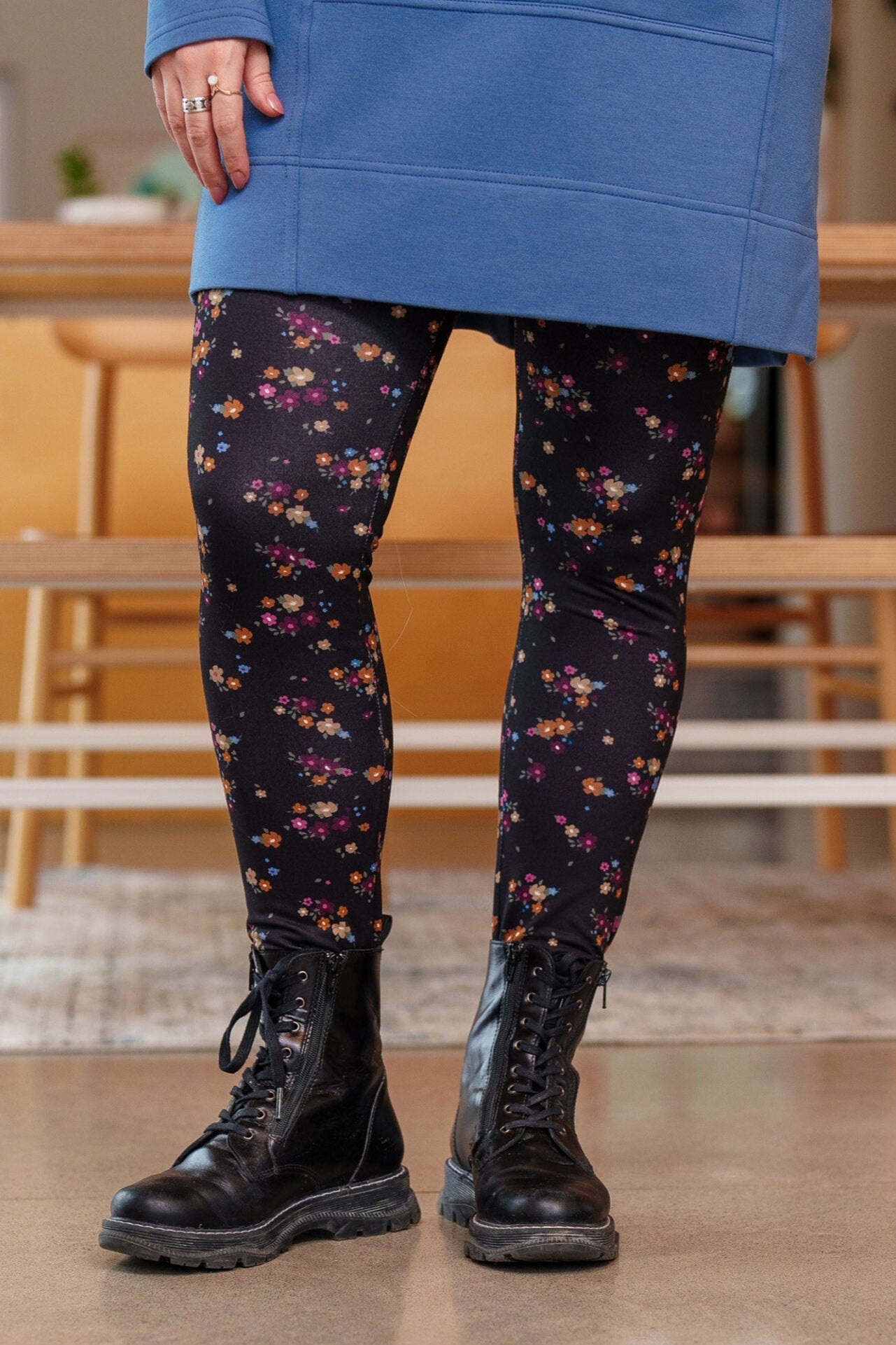 Waist down view of a woman wearing the Laracin Leggings by Rien ne se Perd in a small Floral print, with a blue tunic. She is standing in front of a table. 