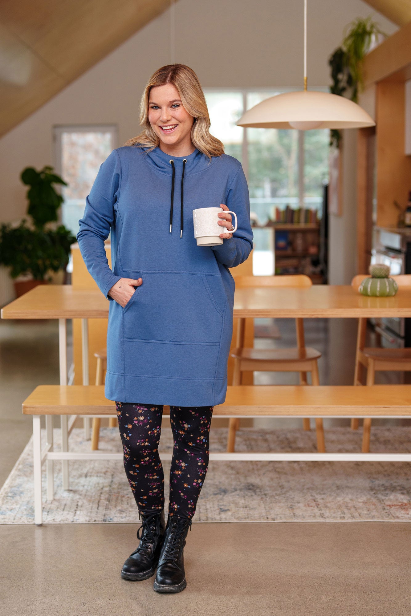 A woman wearing the Laracin Leggings by Rien ne se Perd in a small Floral print, with a blue tunic. She is standing in a kitchen. 