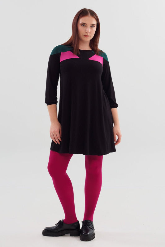 A woman wearing the Dolly Dress by Slak, a Black swing dress with colour-blocking in hot pink and green at the chest and shoulders, with 3/4 sleeves and above the knee length. She is standing in front of a white background. 