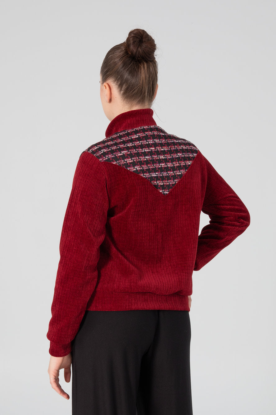 Back view of a woman wearing the Enfield Jacket by Slak, a bomber style jacket in textured burgundy fabric with plaid panels at the sides and across the upper back. She is wearing it with black pants and standing in front of a white background. 