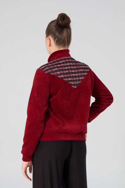 Back view of a woman wearing the Enfield Jacket by Slak, a bomber style jacket in textured burgundy fabric with plaid panels at the sides and across the upper back. She is wearing it with black pants and standing in front of a white background. 