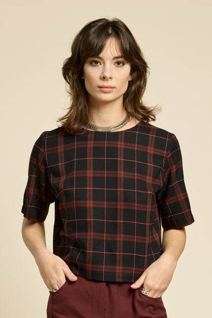 A woman wearing the Soul Love Top by Cokluch in Burgundy Plaid, with a round neck, loose fit, and elbow length sleeves. She is wearing it with with burgundy pants and standing against a beige background.