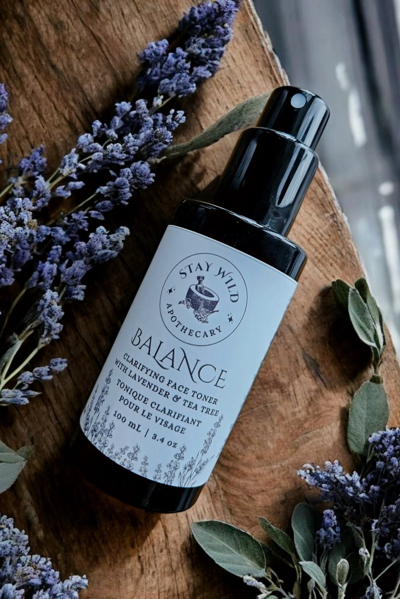 Bottle of 'Balance' face mist by Stay Wild Apothecary shown with lavender flowers on a wooden surfac