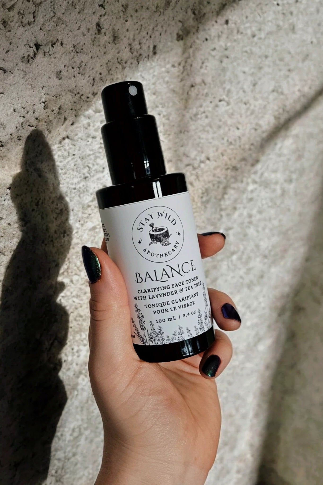 Hand holding a bottle of 'Balance' face mist by Stay Wild Apothecary against a textured wall.