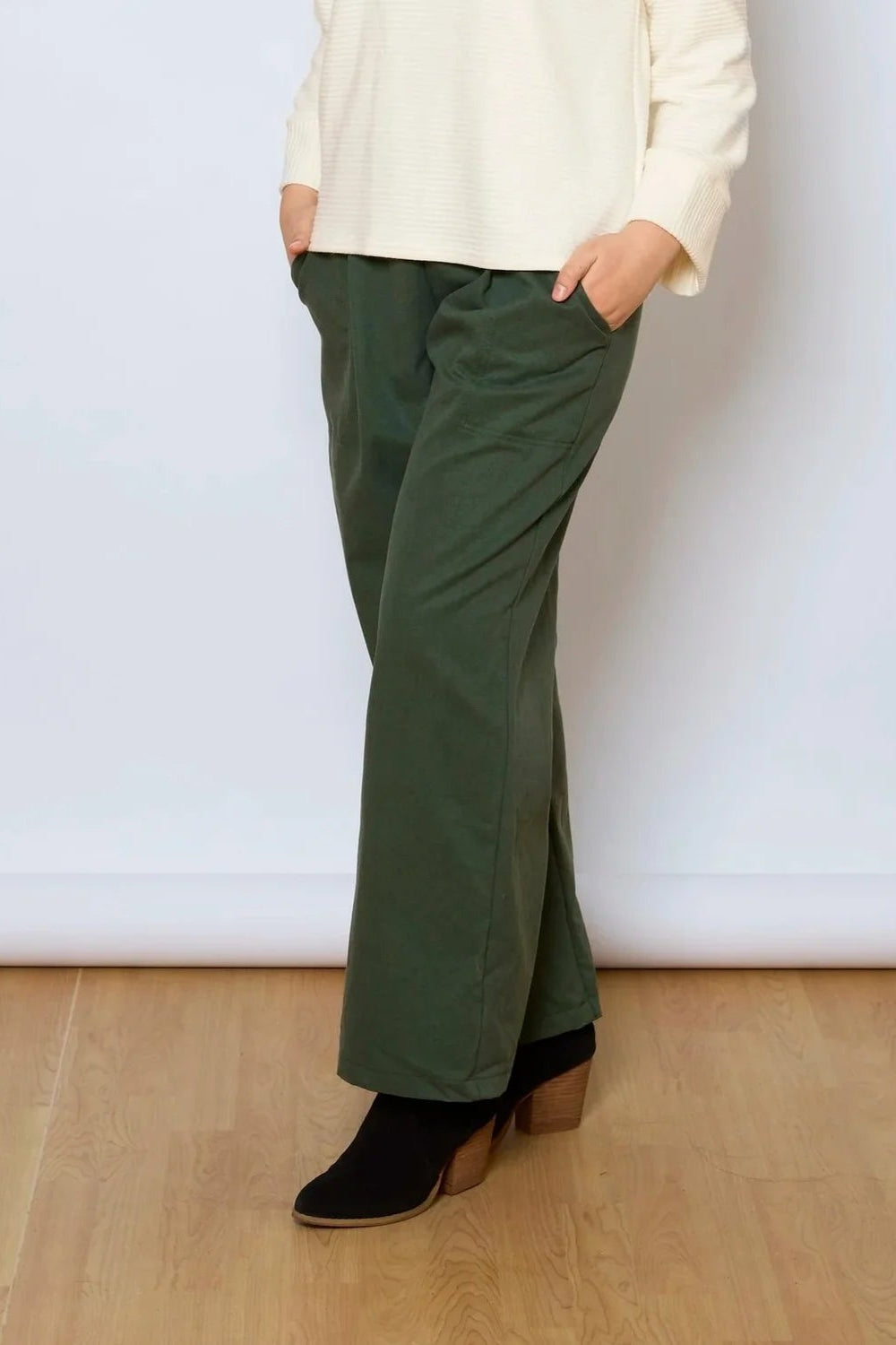Waist down view of a woman wearing the Jill Pants by Tangente in Green, wide-legged ankle length pants with large pockets. She is wearing them with a white sweater against a white background.