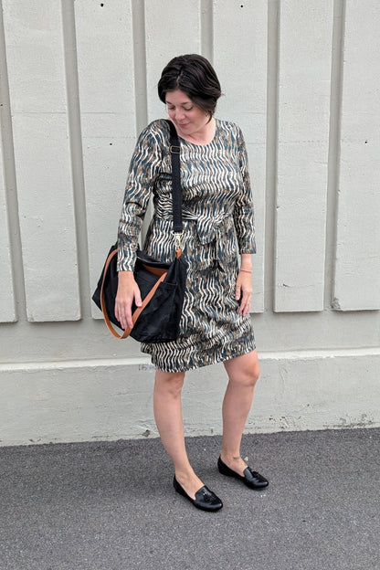 A woman wearing the Gwen Dress by Tangente in Green print, standing outside in front of a white wall

